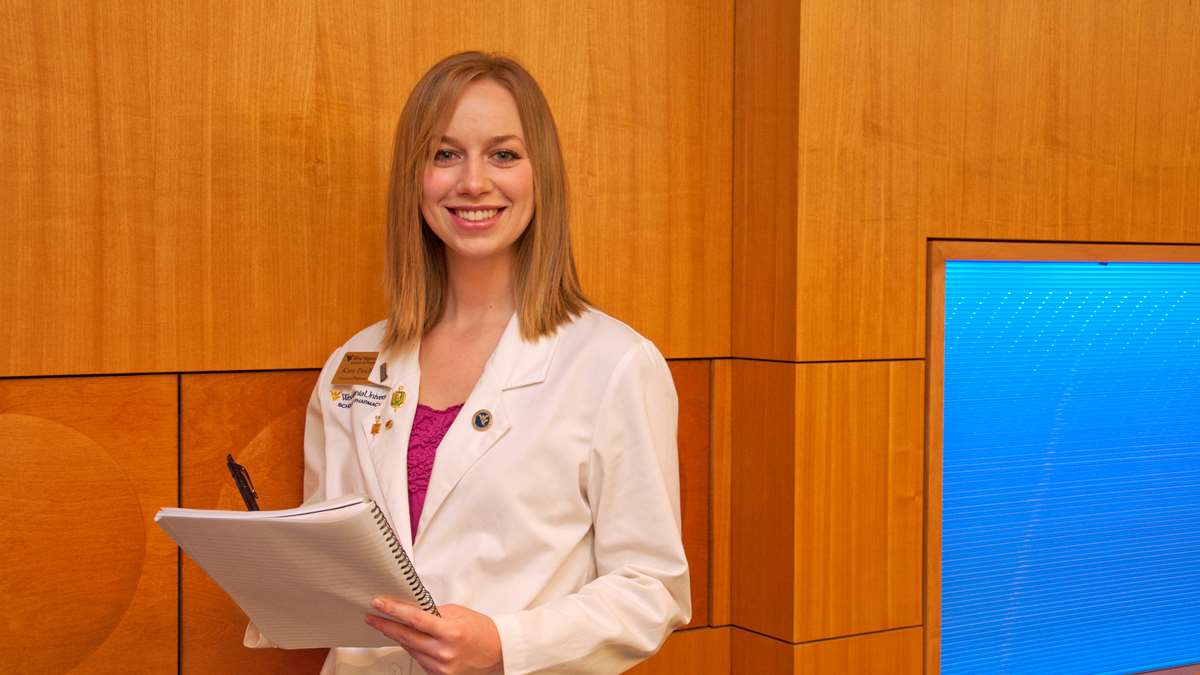 Kara in a white coat with a pen and paper in her hands.