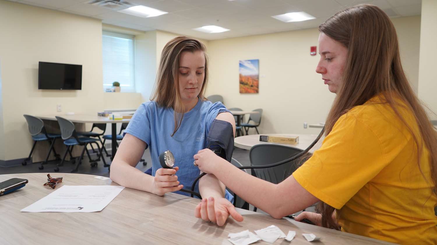 Two female students practice taking blood pressure.