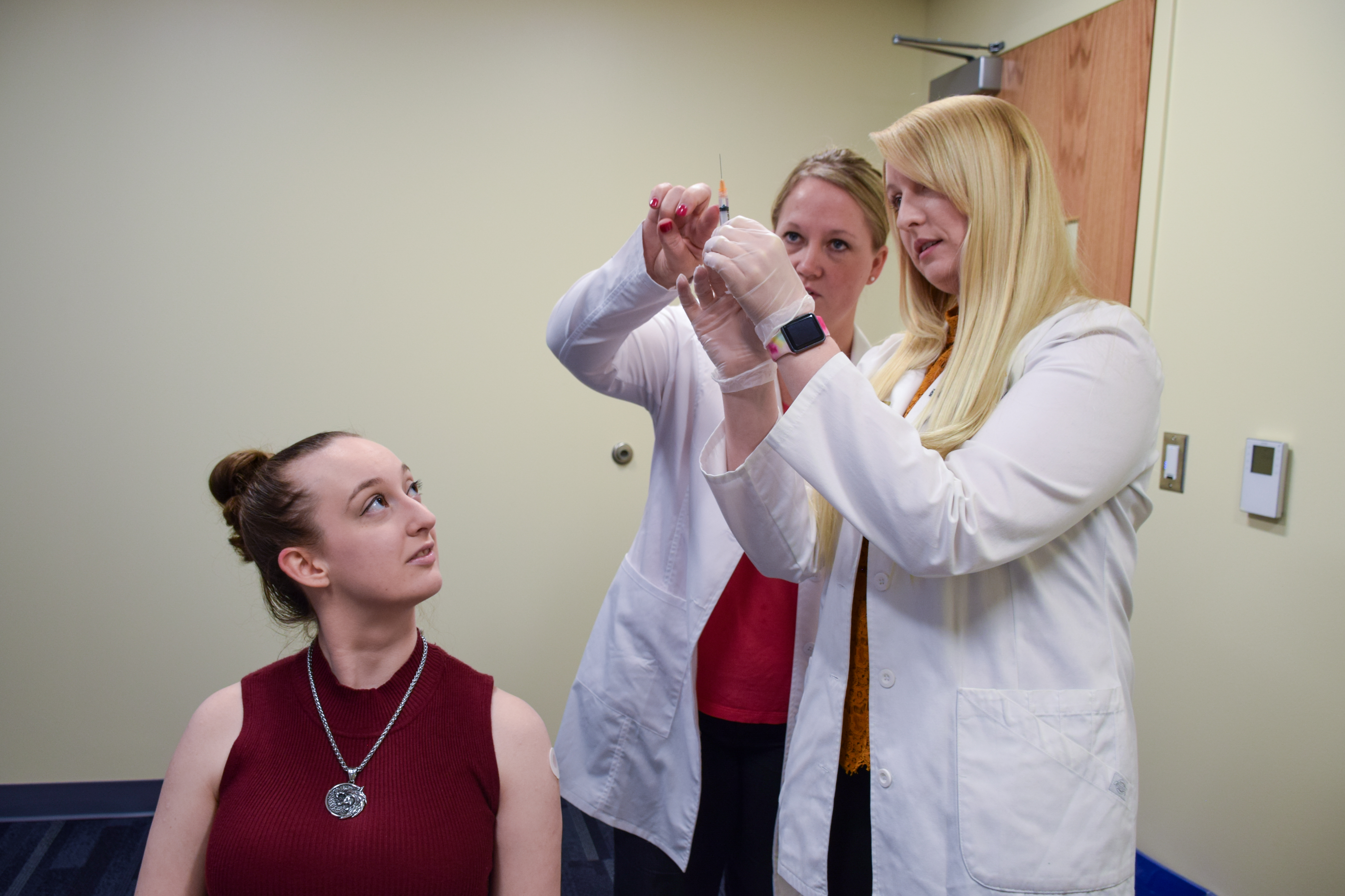 A female professor teaches to female students how to immunize a patient.