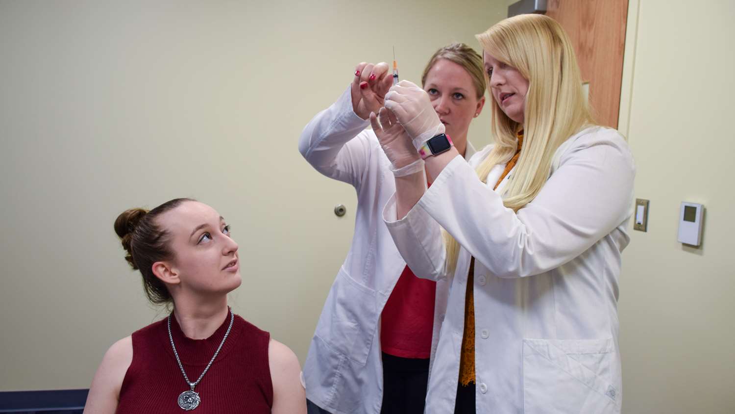 A female professor teaches to female students how to immunize a patient.