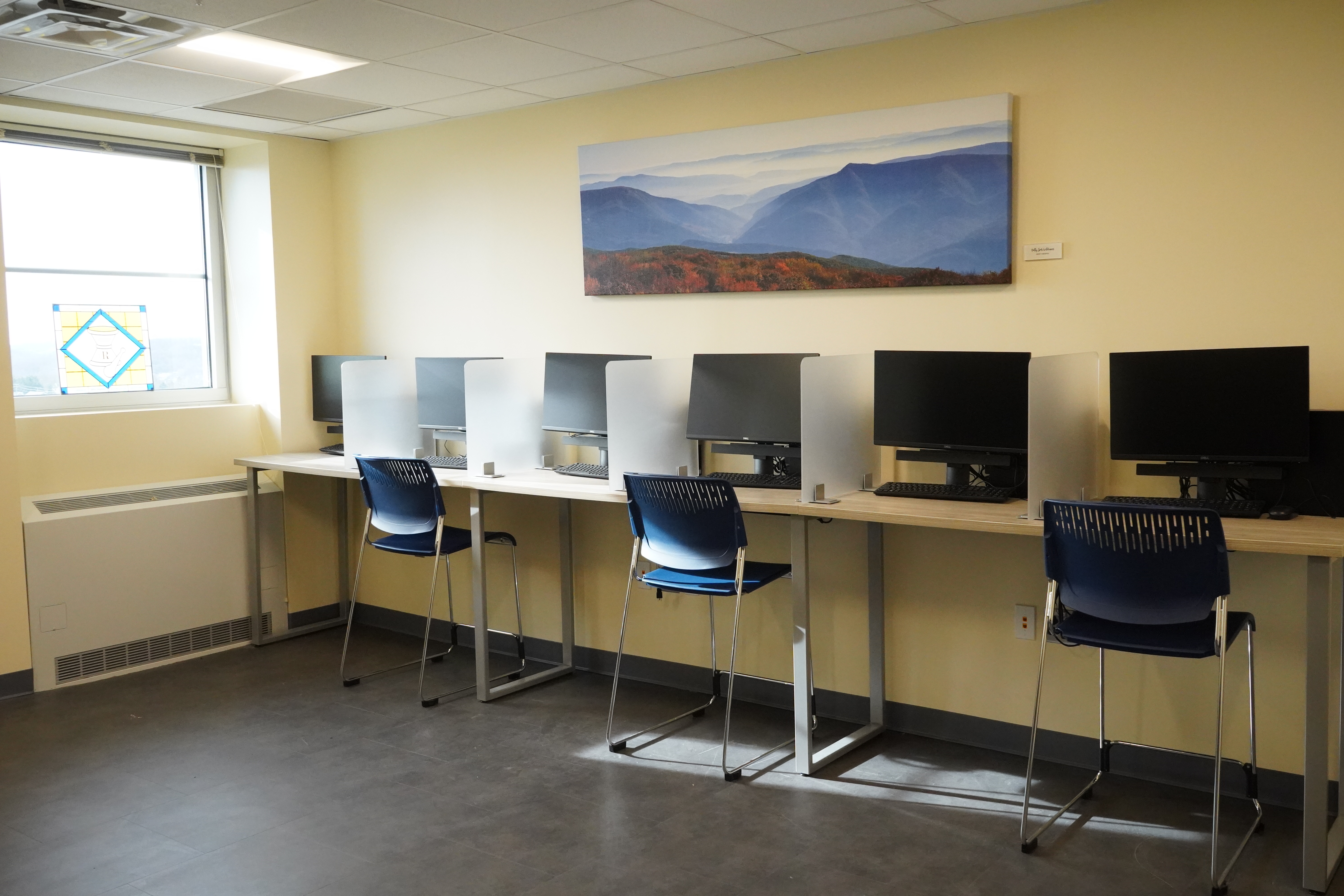 A room with a window and computers against a yellow wall.