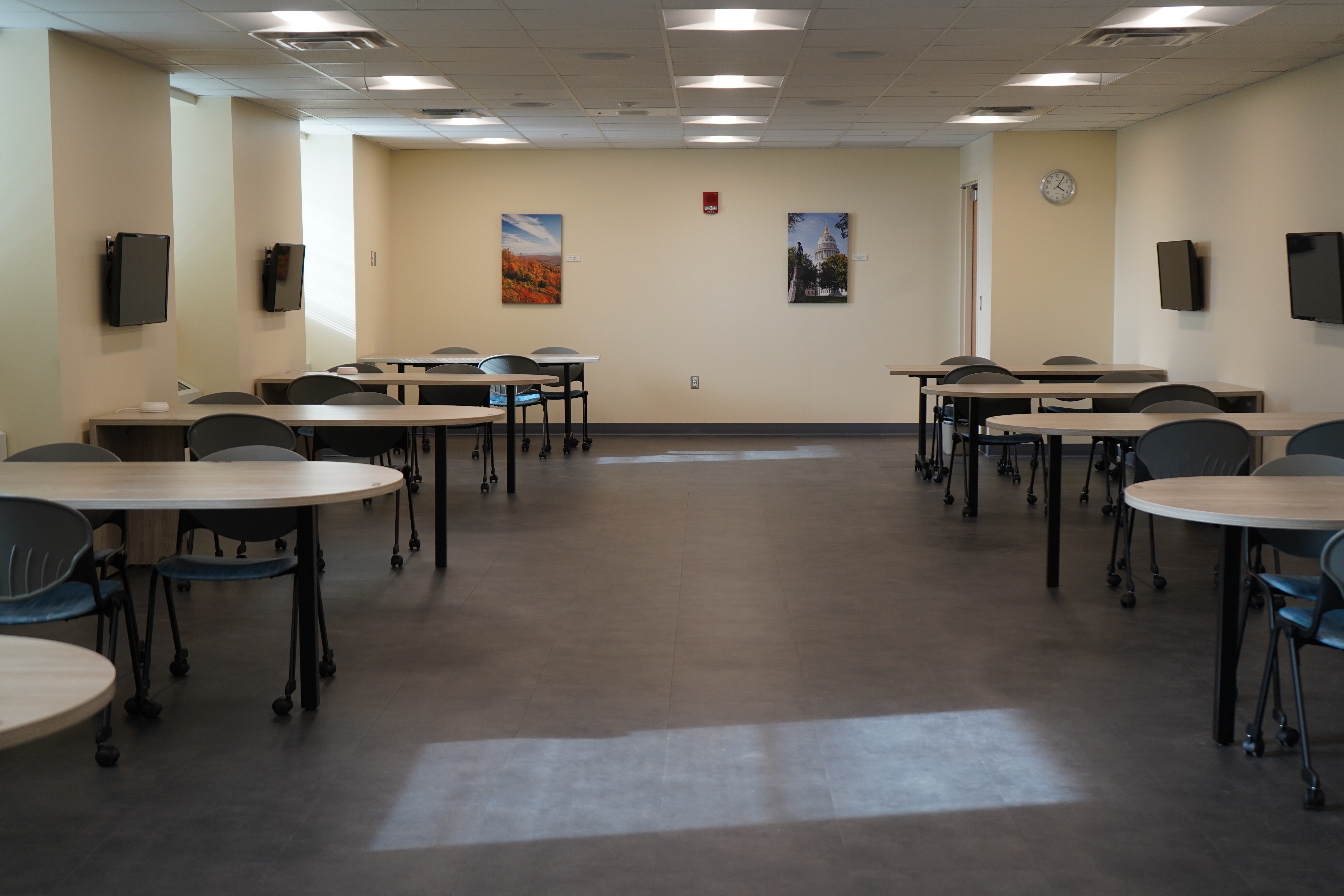 An empty classroom with tables, computers and pictures on the wall.