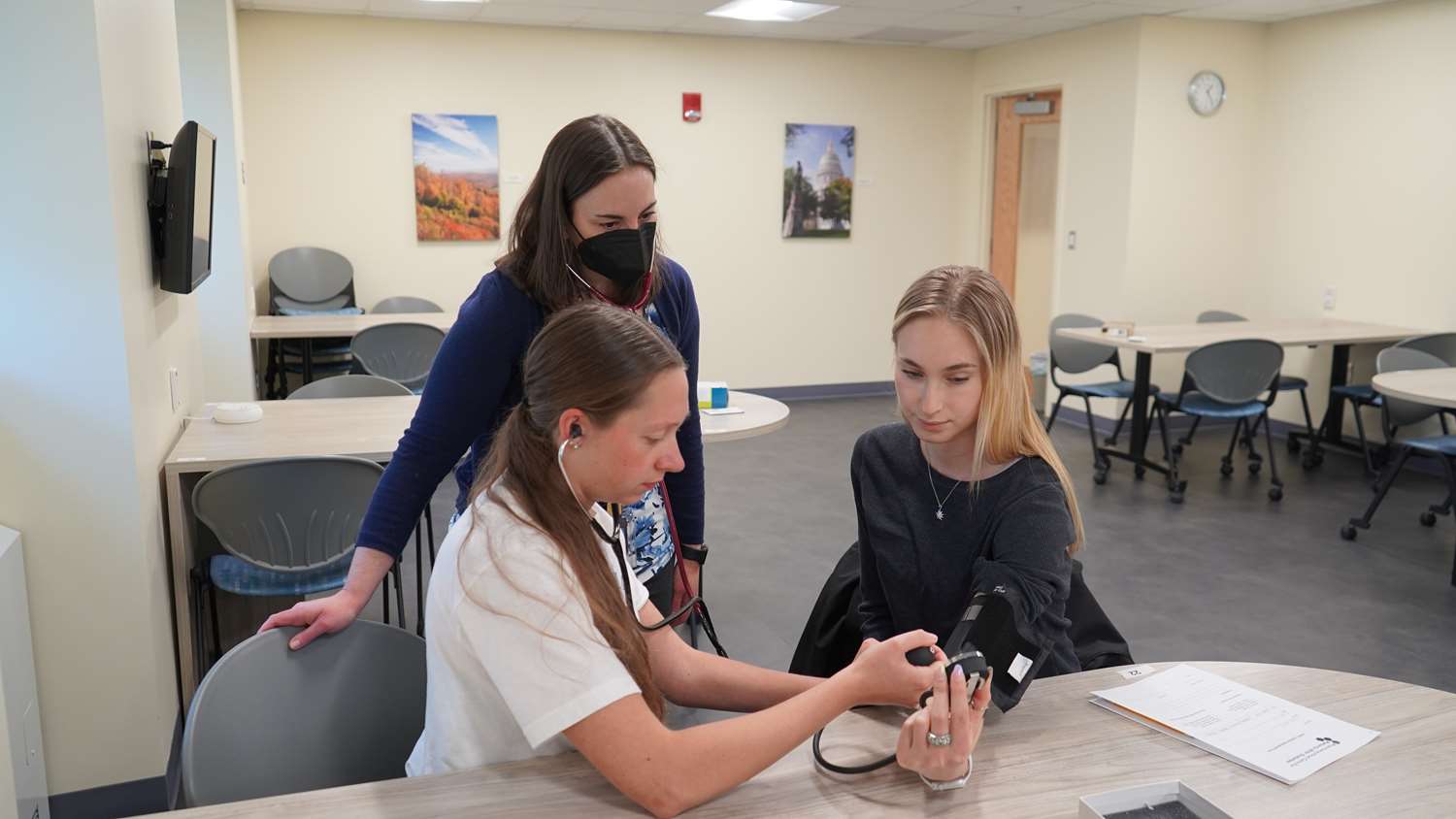 A female professor teaches to female students how to take a patient's blood pressure.
