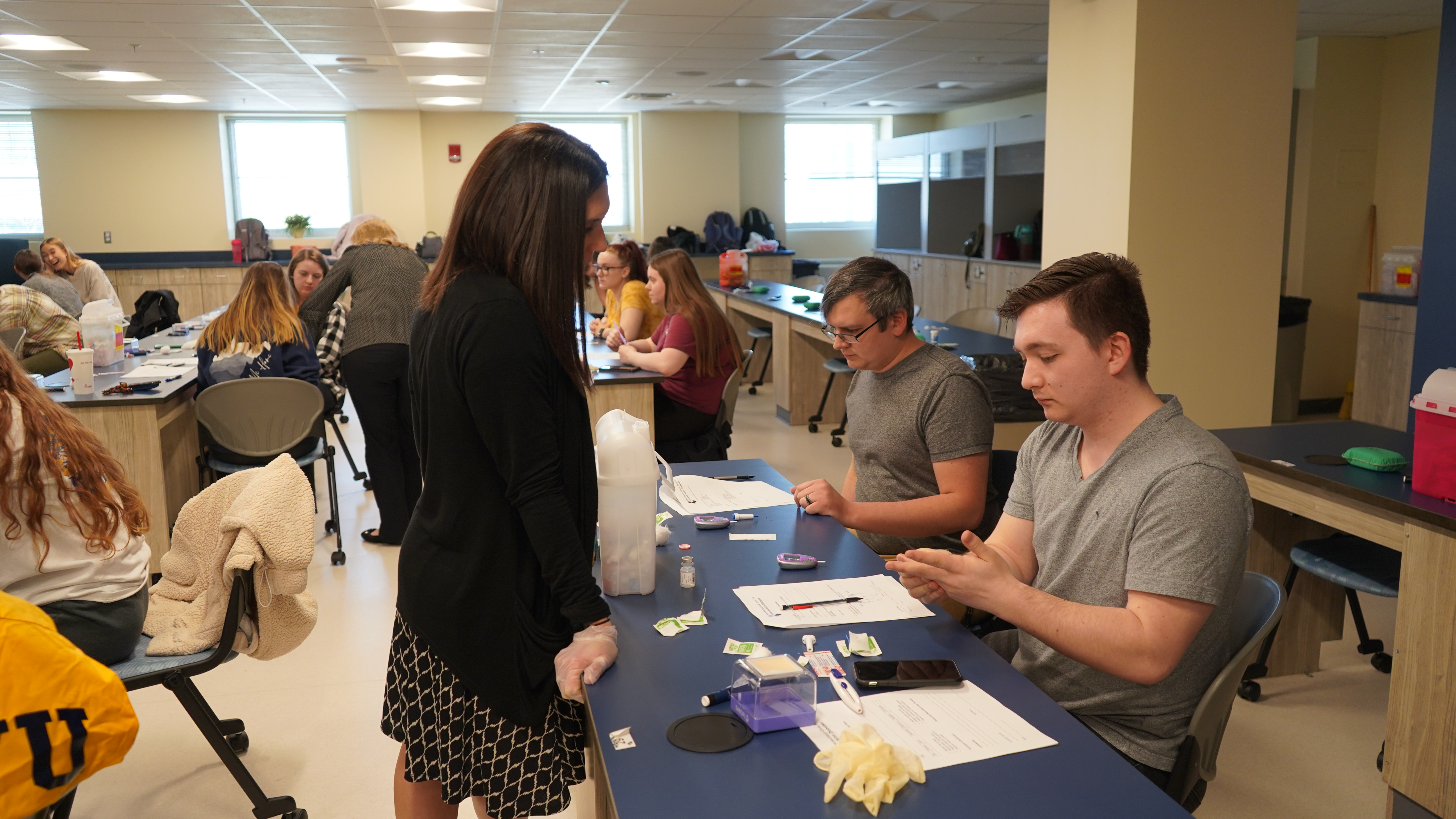 A female professor watches as two male students finish their glucose training.