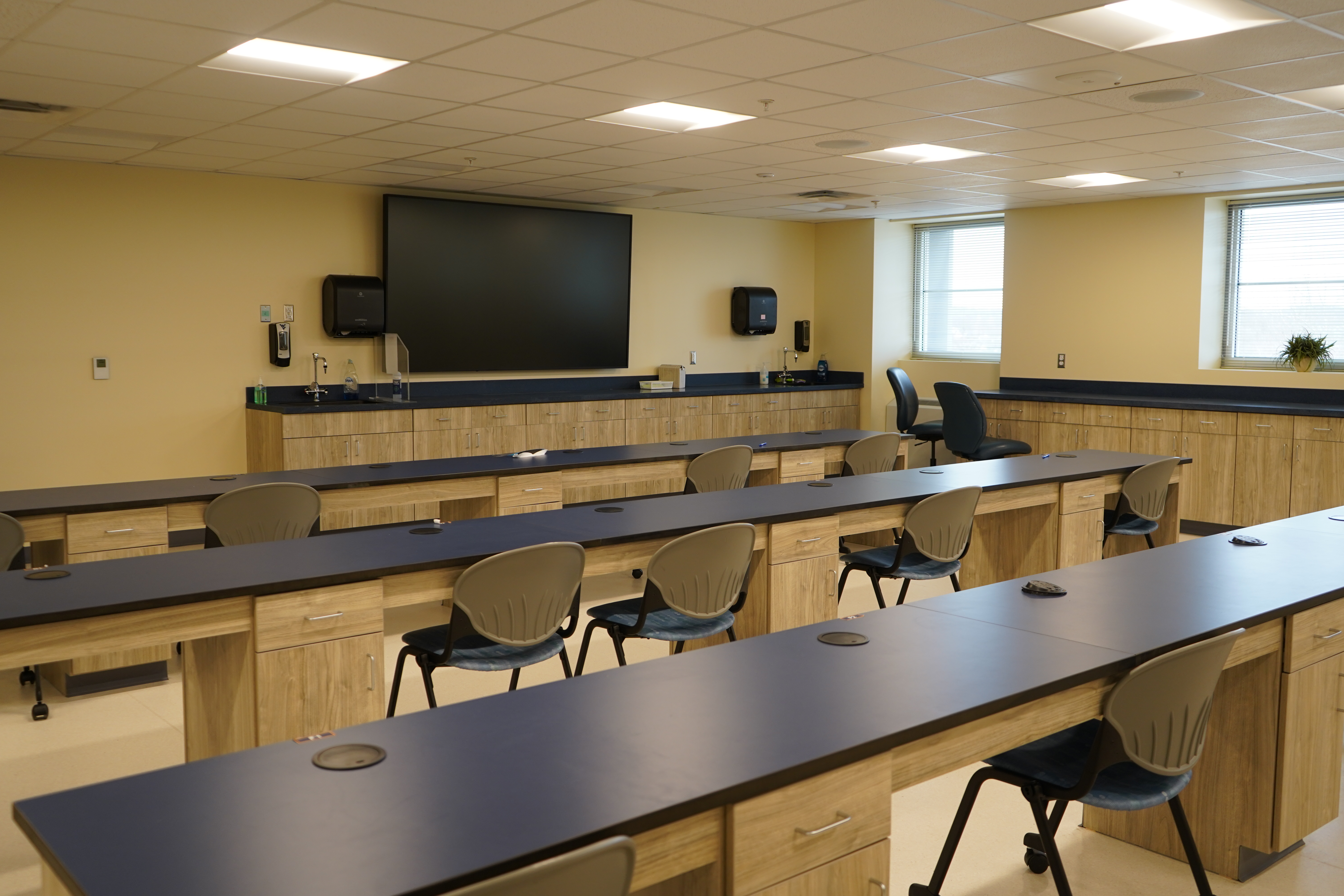 Empty classroom with long tables, chairs and a tv on the wall.