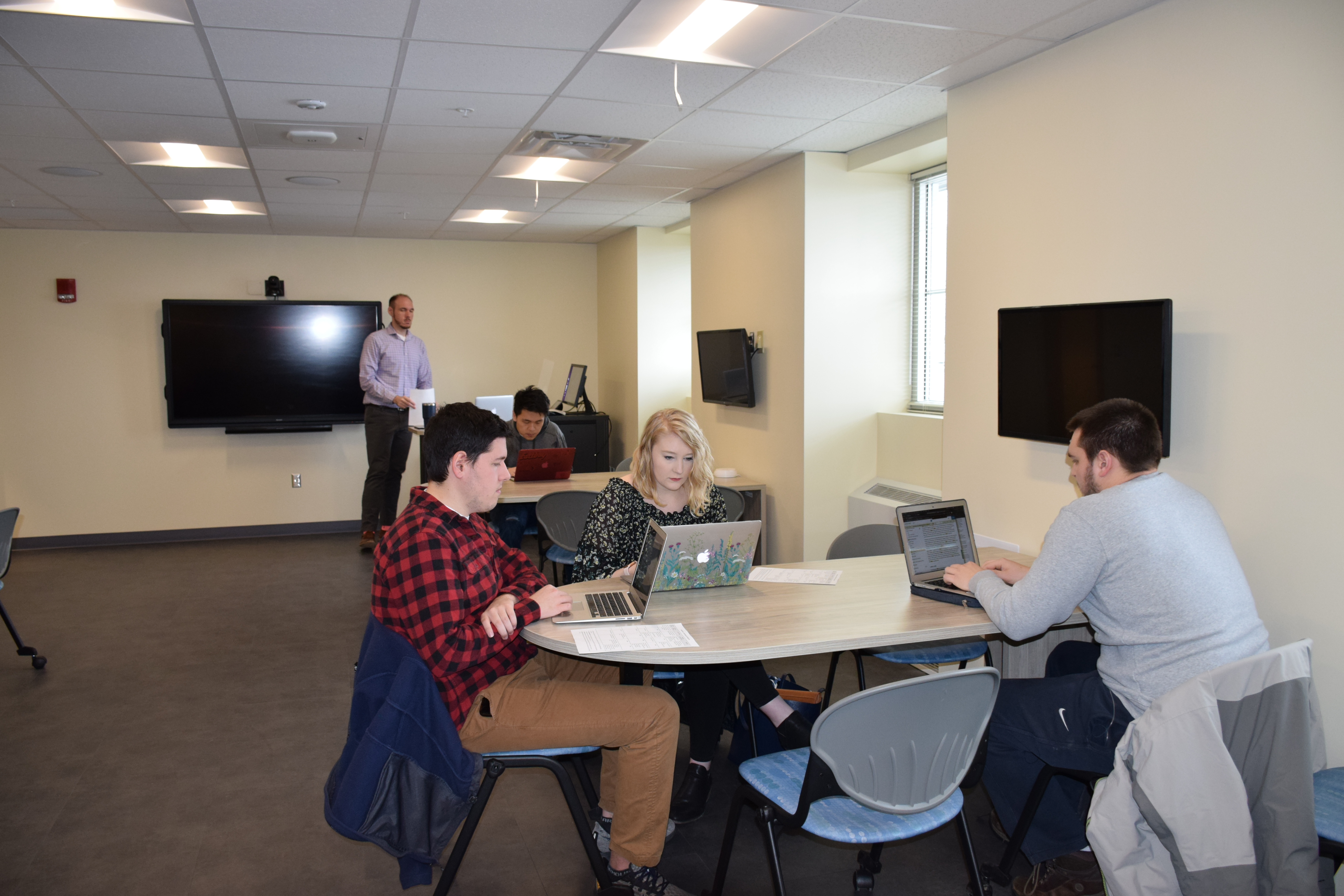 Three students sitting at a table with their laptop computers.