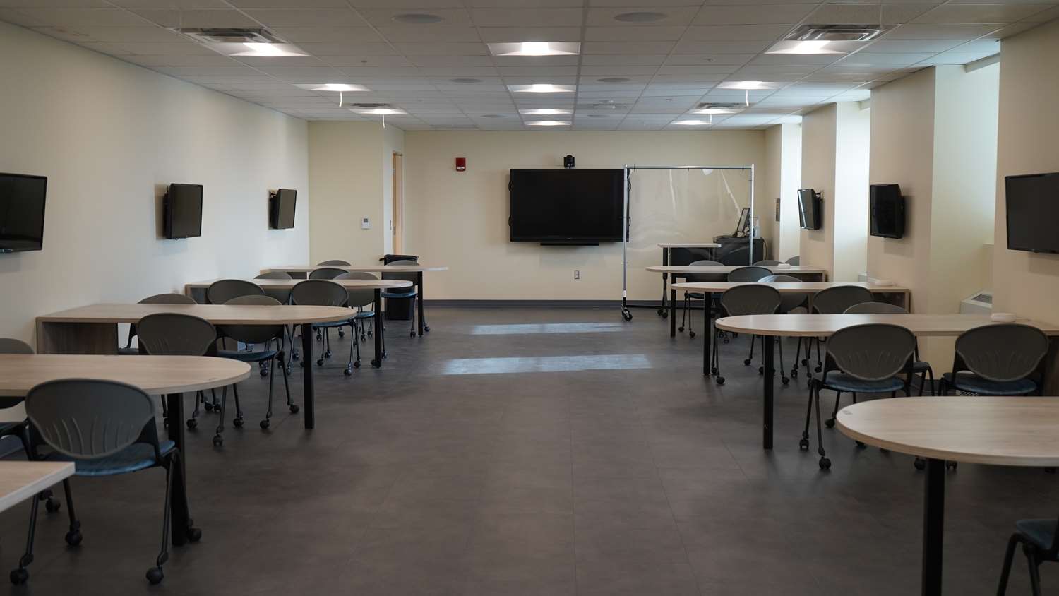 Empty classroom with table, chairs and monitors on the wall.